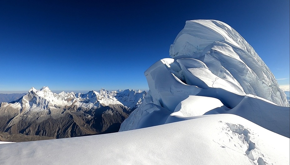 Un alpiniste sur une arête de neige à haute altitude, sous un ciel bleu profond